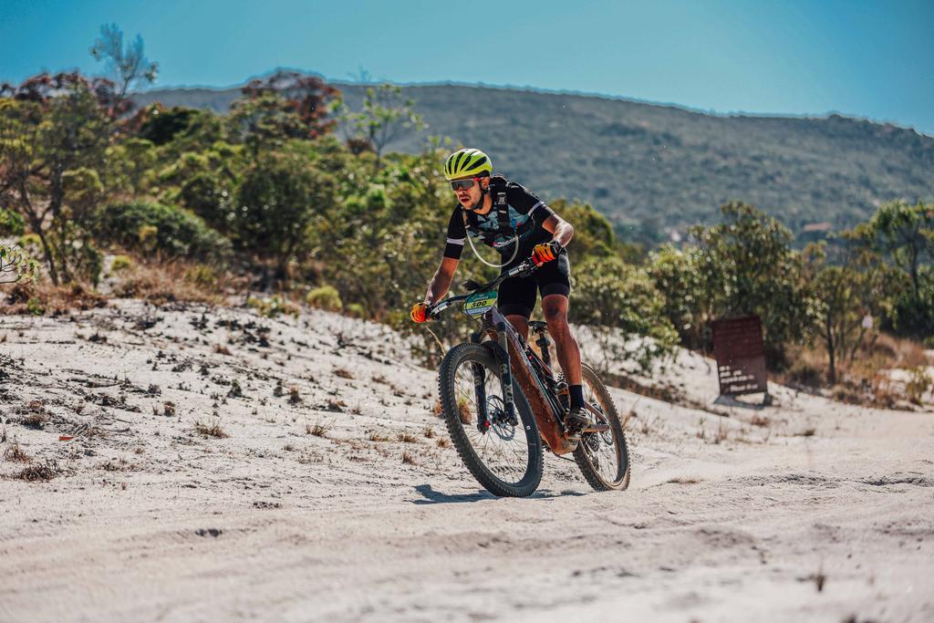 Ciclista em trecho arenoso do Sertões MTB em Ibitipoca, com montanhas ao fundo