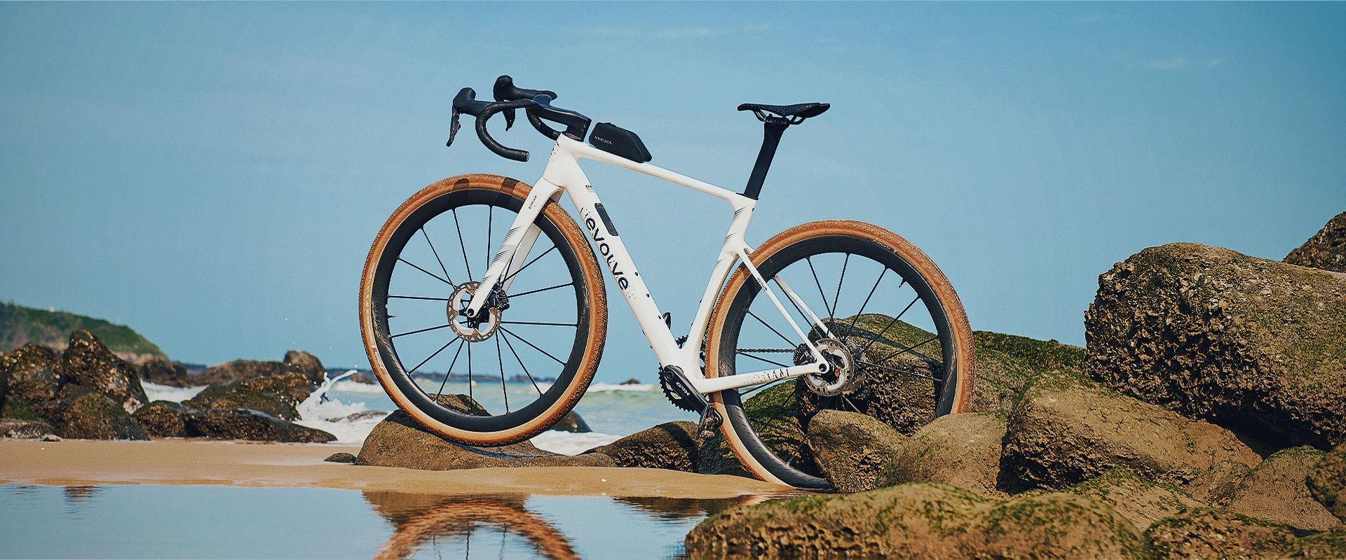 Evolve CIMA GR Sailfish Pearl apoiada em rochas na praia com pneus tan wall
