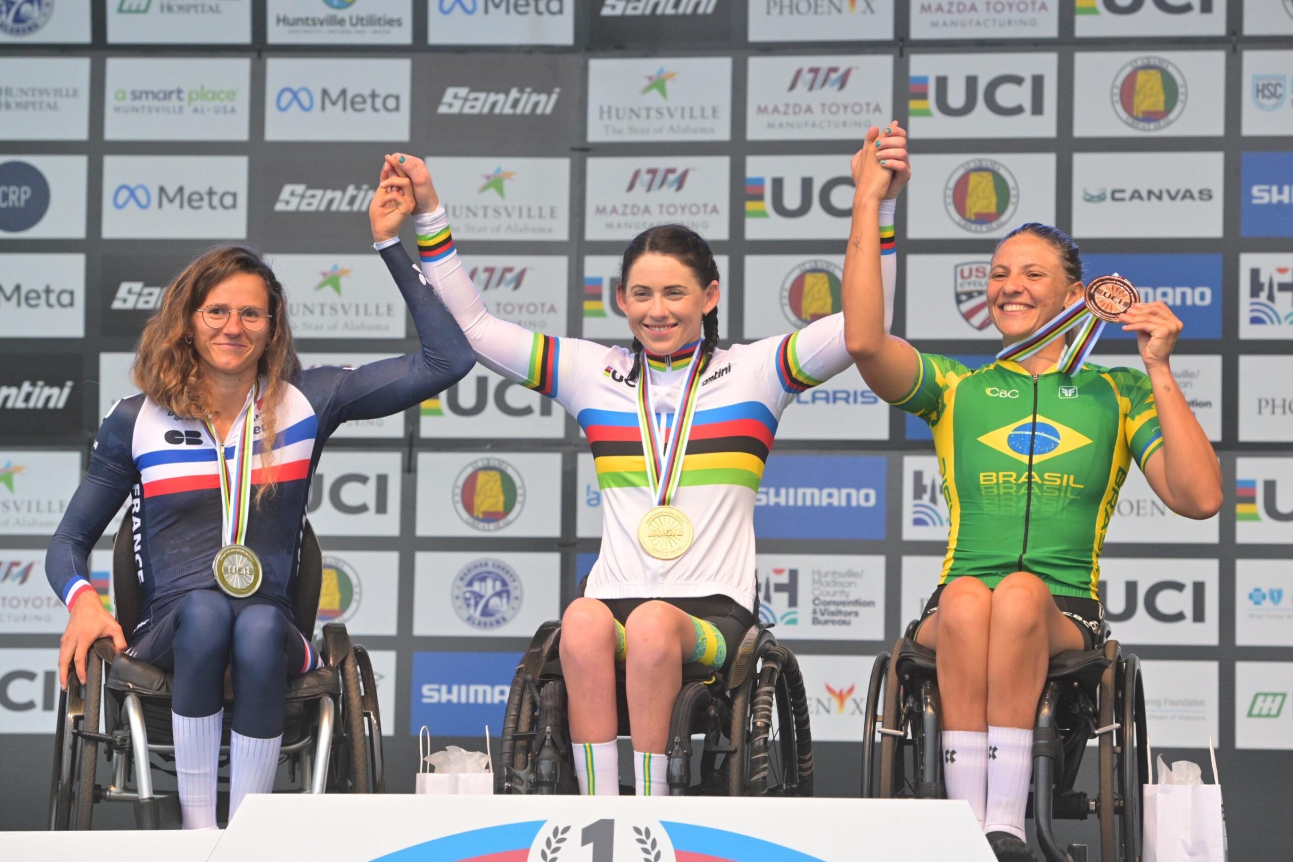 Jéssica Ferreira, à direita, celebra o bronze com Anaïs Vincent e Lauren Parker no pódio WH3 do Mundial de Paraciclismo 2026