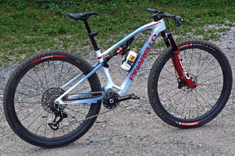 Pinarello Dogma XC de Tom Pidcock, campeão do Mundial de XCO 2026 em Val di Sole — azul GB com fork vermelho RockShox e pneus Vittoria Peyote